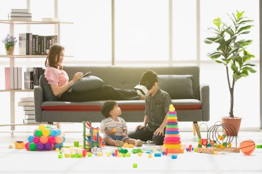 Asya Aile, mutlu zaman evde, genç güzel annem, rahatlatıcı, tablet kullanarak kanepe, Genç çocuk giyim taklit oyun gözlük kulaklık, küçük sevimli yürümeye başlayan çocuk, birlikte oynarken zevk aramak