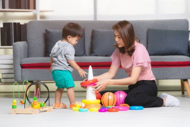 Mutlu Asya Aile, Genç, güzel annesi pembe bluz, yere, oturma içinde sarı ring, gri T-shirt, kısa, sevimli küçük yürümeye başlayan çocuk zevk topla oynamayı ve oyuncaklar oturma odası rahat tutun