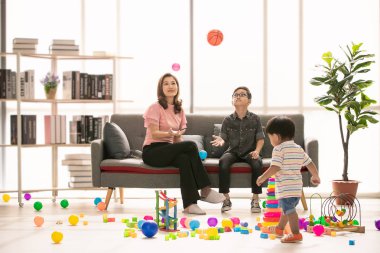 Asya Aile, evde, mutlu zaman genç güzel anne ve genç oğlu koltukta oturan gözler gözlük takan, fırlatma topu, şirin küçük yürümeye başlayan çocuk birlikte modern oturma odasında iskambil çevrede yürüyüş