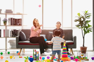 Asya Aile, evde, mutlu zaman genç güzel anne ve genç oğlu koltukta oturan gözler gözlük takan, fırlatma topu, şirin küçük yürümeye başlayan çocuk birlikte modern oturma odasında iskambil çevrede yürüyüş