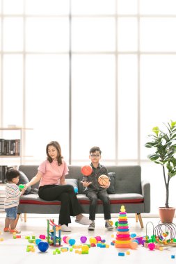 Asya Aile, evde, mutlu zaman genç güzel anne ve genç oğlu koltukta oturan gözler gözlük takan, fırlatma topu, şirin küçük yürümeye başlayan çocuk birlikte modern oturma odasında iskambil çevrede yürüyüş