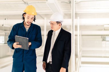 Genç Asyalı mühendis, çalışmalarını sanayi fabrikasındaki kıdemli yönetici mühendise, sanayi fabrikasındaki mevcut iş kavramına sunmak için tablet kullanıyor..