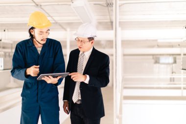 Genç Asyalı mühendis, çalışmalarını sanayi fabrikasındaki kıdemli yönetici mühendise, sanayi fabrikasındaki mevcut iş kavramına sunmak için tablet kullanıyor..