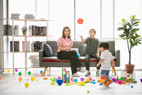 Asya Aile, evde, mutlu zaman genç güzel anne ve genç oğlu koltukta oturan gözler gözlük takan, fırlatma topu, şirin küçük yürümeye başlayan çocuk birlikte modern oturma odasında iskambil çevrede yürüyüş