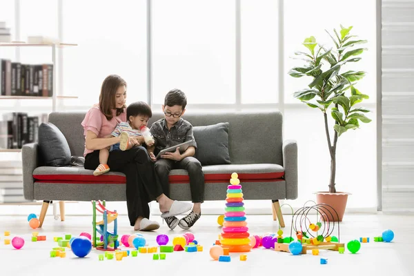 Asya Aile, mutlu, boş zaman evde, genç güzel annem gösteren kitap modern oturma odasında kollarında gözler gözlük takan genç oğlu süt şişeden içme sevimli, küçük yürümeye başlayan çocuk için