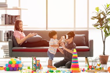 Asya Aile, tablet şakacı kanepeye, Genç çocuk giyim beyaz taklit Oyunlar gözlük kulaklık kullanma ev, genç güzel annem, rahatlatıcı, happy Time'da touch elleriyle küçük sevimli bebek