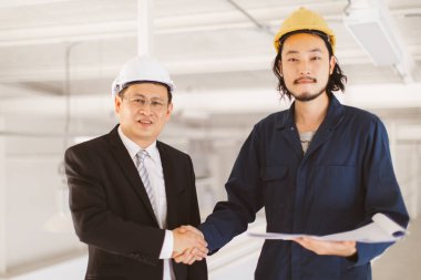 Asyalı yönetici mühendis ve genç mühendis birlikte el sıkışma ve gülümseme yaşlı ayakta elinde plan tutar, sanayi fabrikasında mühendis için kavram.