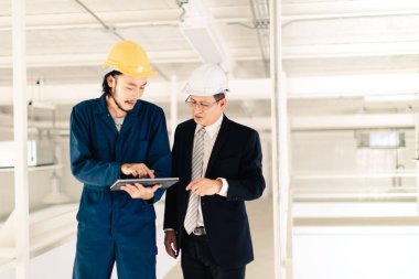 Genç Asyalı mühendis, çalışmalarını sanayi fabrikasındaki kıdemli yönetici mühendise, sanayi fabrikasındaki mevcut iş kavramına sunmak için tablet kullanıyor..