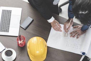 Yakın plan, Asyalı iş adamı ve erkek ustabaşının üst görüntüsü, çizim, bina planı tasarımı, dizüstü bilgisayar, miğfer ve çalışma masasında tartışmalar..