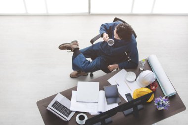 Asya sakal erkek foreman, coverall, üstten görünüm Emanet ayakkabı giymek, sakin ol, sandalye, kahve fincanı tablo, ileti örneği, Emanet kask, dizüstü bilgisayar, tablet, smartphone, office arka plan oturmak