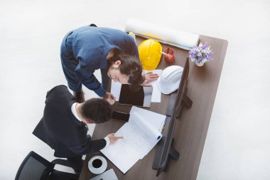 Siyah takım elbiseli Asyalı iş adamının en iyi görüntüsü, çizim yapmakla meşgul, ustabaşıyla konuşuyor, kırtasiye malzemesi, beyaz ve sarı güvenlik kaskı, dizüstü bilgisayar, tablet, akıllı telefon, ofis geçmişi.