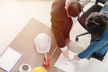 Yakın plan, Asyalı iş adamı ve erkek ustabaşının üst görüntüsü, çizim, bina planı tasarımı, dizüstü bilgisayar, miğfer ve çalışma masasında tartışmalar..