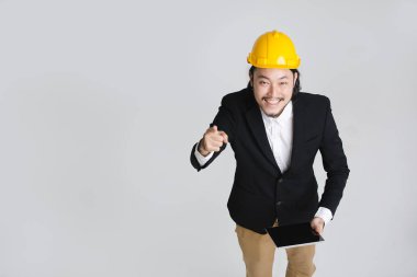 Mutlu, siyah takım elbise ve beyaz gömlek genç Asyalı iş adamı üst görünümü, sarı kask giyen, aşağı bakıyor ve elinde tablet ekranına dokunmadan, beyaz izole arka plan üzerinde