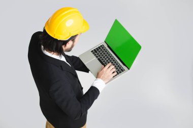 Mutlu, siyah takım elbise ve beyaz gömlek genç Asyalı iş adamı üst görünümü, sarı kask giyen, aşağı bakıyor ve elinde tablet ekranına dokunmadan, beyaz izole arka plan üzerinde