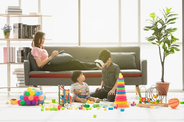 Asya Aile, mutlu zaman evde, genç güzel annem, rahatlatıcı, tablet kullanarak kanepe, Genç çocuk giyim taklit oyun gözlük kulaklık, küçük sevimli yürümeye başlayan çocuk, birlikte oynarken zevk aramak