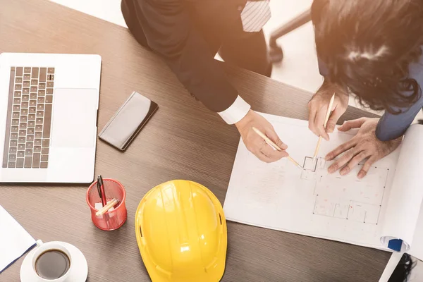 Yakın plan, Asyalı iş adamı ve erkek ustabaşının üst görüntüsü, çizim, bina planı tasarımı, dizüstü bilgisayar, miğfer ve çalışma masasında tartışmalar..