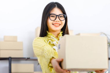 Genç ve çekici Asyalı iş kadını, uzun siyah saçlı, gözlüklü, sarı bluzlu, müşterinin siparişini ve mesajını tekrar kontrol eden, başlangıç ofisinde kutularla dolu.