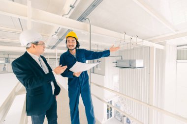 , çok uzak Orta yaş Asya fabrika yöneticisi ve genç Asya mühendisi kot tulum, güvenlik ayakkabıları, kask üretim tesisinin çatısında bir şey noktası