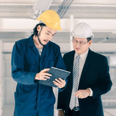 Genç Asyalı mühendis, çalışmalarını sanayi fabrikasındaki kıdemli yönetici mühendise, sanayi fabrikasındaki mevcut iş kavramına sunmak için tablet kullanıyor..