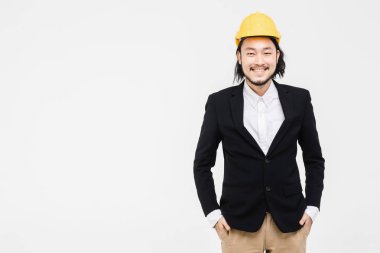 Asyalı mühendisportresi, siyah takım elbiseli, başında sarı kask, ayakta, arkasında beyaz arka plan.