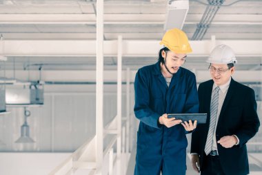 Genç Asyalı mühendis, çalışmalarını sanayi fabrikasındaki kıdemli yönetici mühendise, sanayi fabrikasındaki mevcut iş kavramına sunmak için tablet kullanıyor..