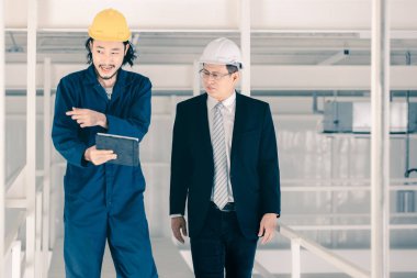 Genç Asyalı mühendis, çalışmalarını sanayi fabrikasındaki kıdemli yönetici mühendise, sanayi fabrikasındaki mevcut iş kavramına sunmak için tablet kullanıyor..