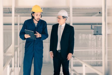 Genç Asyalı mühendis, çalışmalarını sanayi fabrikasındaki kıdemli yönetici mühendise, sanayi fabrikasındaki mevcut iş kavramına sunmak için tablet kullanıyor..