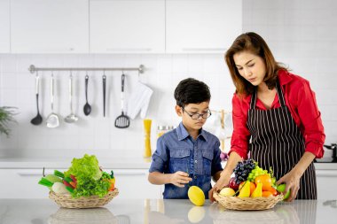 Asyalı anne ve çocuk sepette sebze ve meyve depolamak için öğrenirler. Lüks mutfakta yıkandıktan sonra.