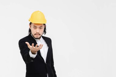 Asyalı mühendis portresi, siyah takım elbiseli, başında sarı kask, ayakta ve el öne çıkıyor, arkasında beyaz arka plan.
