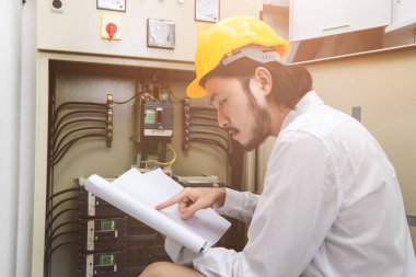 Genç Asyalı elektrik mühendisi bej pantolon ve beyaz gömlek, yakın çekim, Sarı kask, öğretim el çalışma Denetim Masası bodur takmak, onun rutin günlük kontrol izleyin