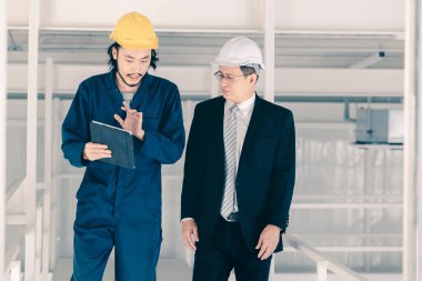 Genç Asyalı mühendis, çalışmalarını sanayi fabrikasındaki kıdemli yönetici mühendise, sanayi fabrikasındaki mevcut iş kavramına sunmak için tablet kullanıyor..