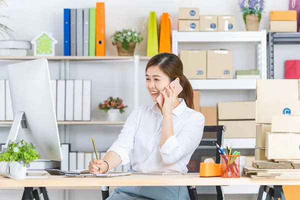 Midilli kuyruk, beyaz gömlek, oturma, gülümseyen yüz ile genç güzel, çekici Asyalı iş kadını Portresi, müşteri ile akıllı telefon konuşurken not alma, başlangıç ofis arka planda