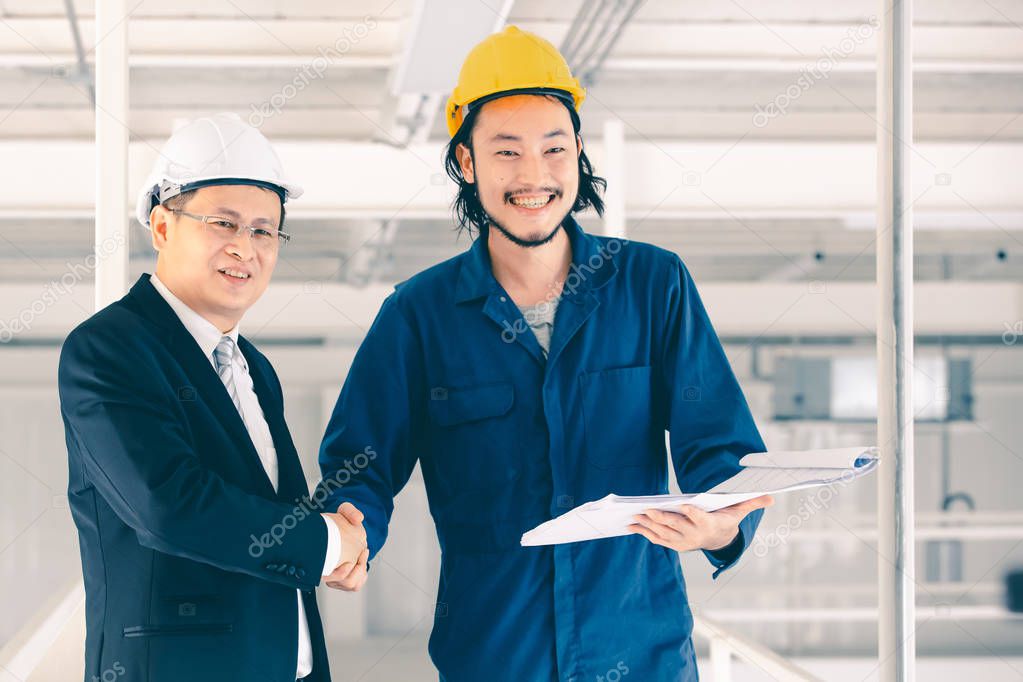 Young Asian engineer handshakes with executive engineer  in industrial factory, blueprint inyoung engineer hand, concept for boss comes visit industrial factory.