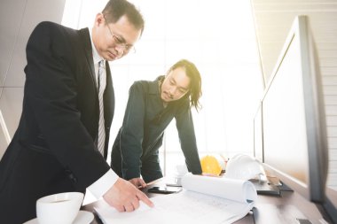 Takım elbiseli genç mühendis modern ofisteki plan tasarımı konusunda kıdemli mühendis patronla görüşüyor..