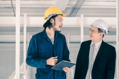 Genç Asyalı mühendis, çalışmalarını sanayi fabrikasındaki kıdemli yönetici mühendise, sanayi fabrikasındaki mevcut iş kavramına sunmak için tablet kullanıyor..