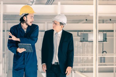 Genç Asyalı mühendis, çalışmalarını sanayi fabrikasındaki kıdemli yönetici mühendise, sanayi fabrikasındaki mevcut iş kavramına sunmak için tablet kullanıyor..