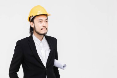 Gülümseme Asyalı mühendis portresi, siyah takım elbiseli, başında sarı kask, ayakta ve kolunda plan tuck, arkasında beyaz arka plan.