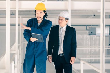 Genç Asyalı mühendis, çalışmalarını sanayi fabrikasındaki kıdemli yönetici mühendise, sanayi fabrikasındaki mevcut iş kavramına sunmak için tablet kullanıyor..
