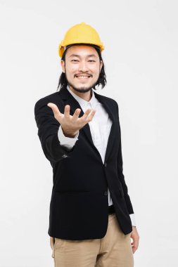 Asyalı mühendis portresi, siyah takım elbiseli, başında sarı kask, ayakta ve el öne çıkıyor, arkasında beyaz arka plan.