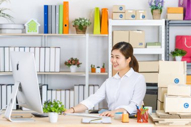 Midilli kuyruklu, beyaz tişörtlü, bilgisayarın önünde oturan, gülümseyen yüzlü, müşterilerden ve tedarikçilerden gelen e-postaları kontrol eden yakışıklı, çekici Asyalı iş kadını.