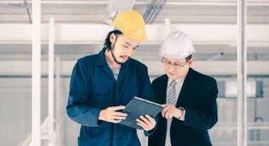 Genç Asyalı mühendis, çalışmalarını sanayi fabrikasındaki kıdemli yönetici mühendise, sanayi fabrikasındaki mevcut iş kavramına sunmak için tablet kullanıyor..