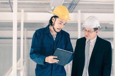 Genç Asyalı mühendis, çalışmalarını sanayi fabrikasındaki kıdemli yönetici mühendise, sanayi fabrikasındaki mevcut iş kavramına sunmak için tablet kullanıyor..