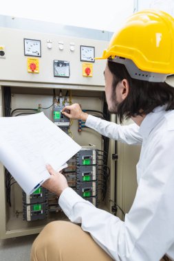 Genç Asyalı elektrik mühendisi bej pantolon ve beyaz gömlek, yakın çekim, Sarı kask, öğretim el çalışma Denetim Masası bodur takmak, onun rutin günlük kontrol izleyin