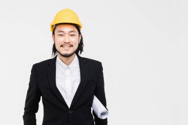 Gülümseme Asyalı mühendis portresi, siyah takım elbiseli, başında sarı kask, ayakta ve kolunda plan tuck, arkasında beyaz arka plan.