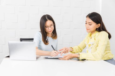 Shot iki genç, güzel, Asyalı mimarlar, proje planlama tartışmak, şantiye toplantı odasında, not defterine yazma, dizüstü bilgisayar, tablet ve beyaz tuğla duvar arka plan ile