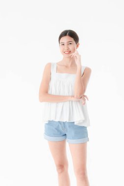 Stüdyo portre rahat yaz kıyafetler, kot şort ve gevşek kolsuz bluz, geniş bir gülümseme, genç güzel, çekici Asya kadının ayakta, izole beyaz arka plan üzerinde poz