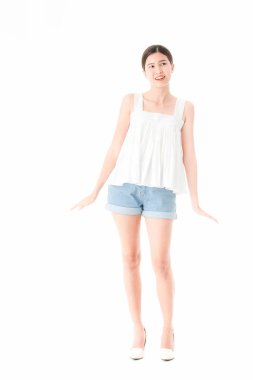 Stüdyo portre rahat yaz kıyafetler, kot şort ve gevşek kolsuz bluz, geniş bir gülümseme, genç güzel, çekici Asya kadının ayakta, izole beyaz arka plan üzerinde poz