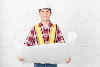 Turuncu, sarı yansıtıcı Emanet yelek ve kask, planları, inşaat site ofiste çalışan kontrol giyen Asya yakışıklı mimar, kot pantolon ve ekose desenli gömlek, orta yaşlı