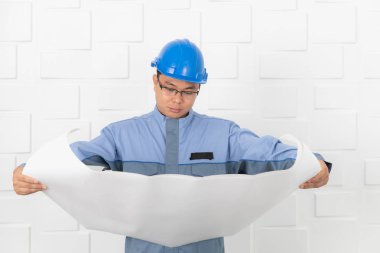 Orta yaşlı, Asya elektrikçi veya içinde tulum, üniforma, giyiyor mavi emniyet kask, çalışma İnşaat çizim, taslakları, beyaz ofis arka planda çalışan teknisyeni varoluş portresi