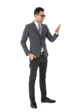 Genç, yakışıklı, Asyalı, işadamıtam uzunlukta portre, iş elbisesi gözlük giyen, ayakta, gülümseyen, izole beyaz arka plan üzerinde, metin mesajı göndermek için akıllı telefon kullanarak